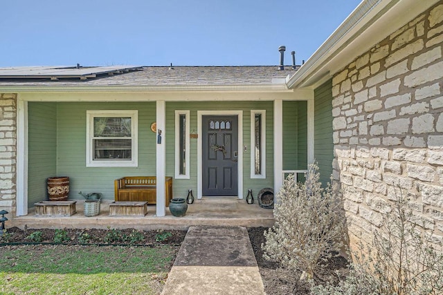 property entrance with stone siding, roof mounted solar panels, covered porch, and a shingled roof