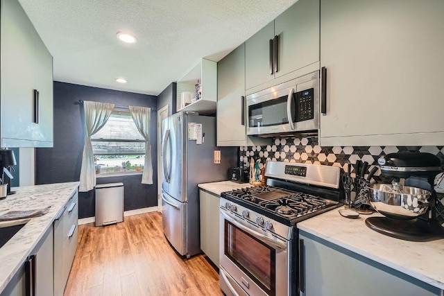 kitchen with light wood-type flooring, backsplash, a textured ceiling, stainless steel appliances, and baseboards