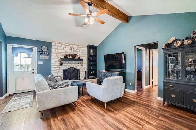 living area with wood finished floors, baseboards, lofted ceiling with beams, a fireplace, and ceiling fan