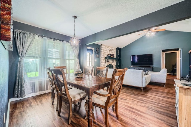 dining room featuring a stone fireplace, vaulted ceiling with beams, a ceiling fan, and wood finished floors