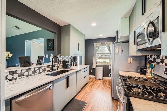 kitchen with light wood finished floors, visible vents, stainless steel appliances, a textured ceiling, and a sink