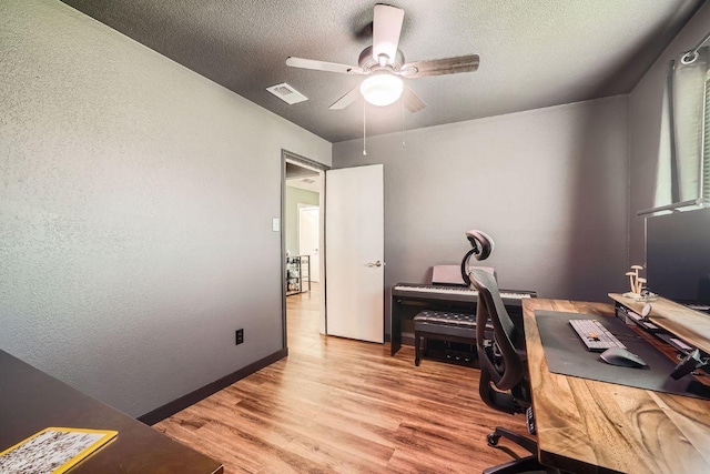 office featuring a ceiling fan, light wood-style floors, visible vents, and a textured ceiling