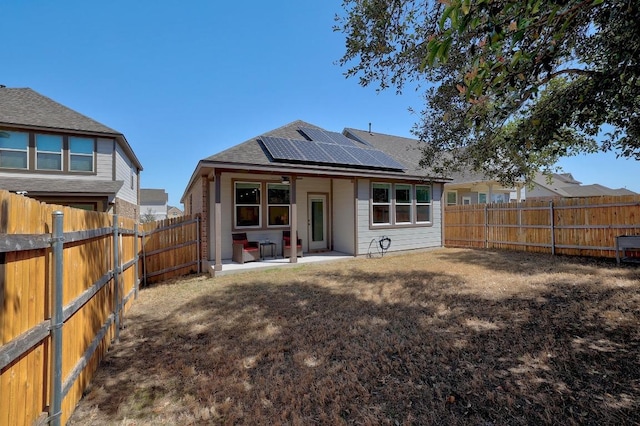 rear view of house featuring a patio, a fenced backyard, and roof mounted solar panels