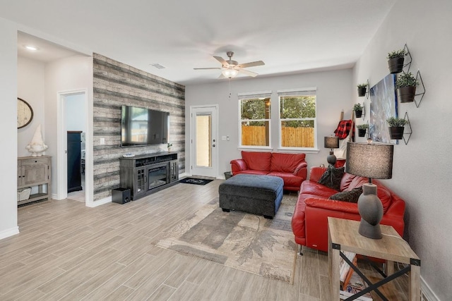 living room with visible vents, light wood-style flooring, a ceiling fan, and baseboards