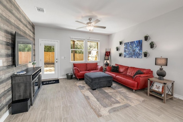 living room featuring light wood finished floors, visible vents, baseboards, and ceiling fan