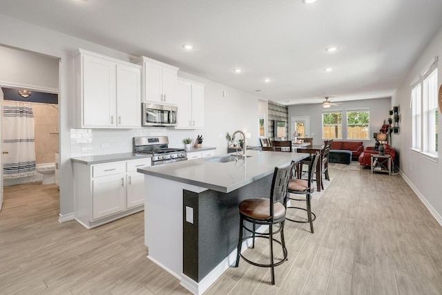 kitchen featuring a kitchen bar, an island with sink, a sink, open floor plan, and appliances with stainless steel finishes