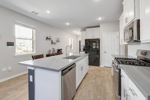 7505 Albany Dr, Austin, TX 78754 - kitchen featuring stainless steel appliances, light wood-style floors, a kitchen island with sink, backsplash, and white cabinets
