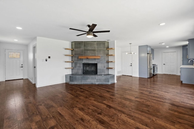 unfurnished living room with ceiling fan, a tiled fireplace, baseboards, dark wood-type flooring, and recessed lighting