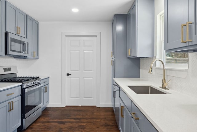 kitchen with gray cabinets, a sink, tasteful backsplash, dark wood finished floors, and appliances with stainless steel finishes