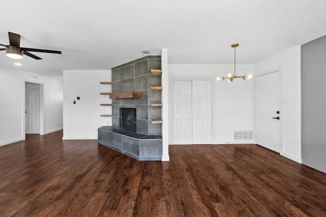 unfurnished living room with visible vents, dark wood-type flooring, baseboards, ceiling fan with notable chandelier, and a tile fireplace