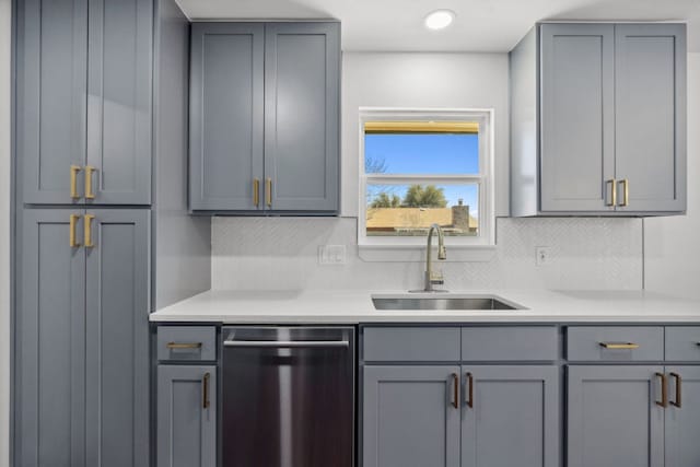 kitchen featuring tasteful backsplash, light countertops, gray cabinets, stainless steel dishwasher, and a sink