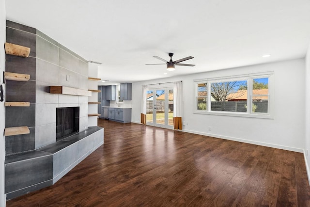 unfurnished living room with dark wood-type flooring, french doors, baseboards, ceiling fan, and a tile fireplace