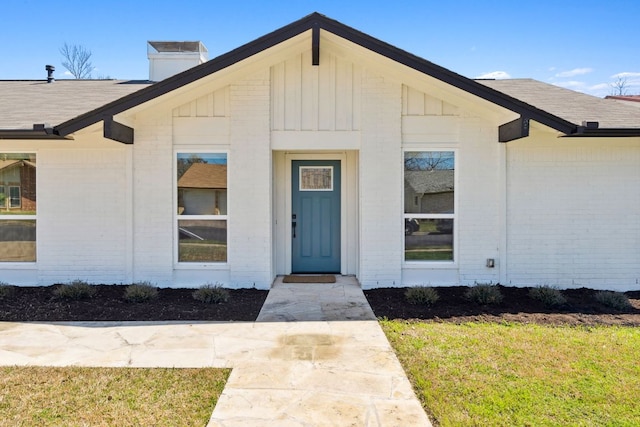 entrance to property featuring board and batten siding, a lawn, a chimney, and brick siding