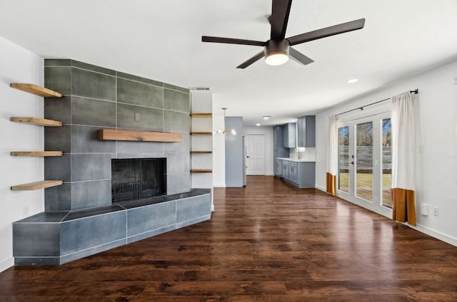 unfurnished living room featuring ceiling fan, french doors, dark wood-style floors, and a tiled fireplace