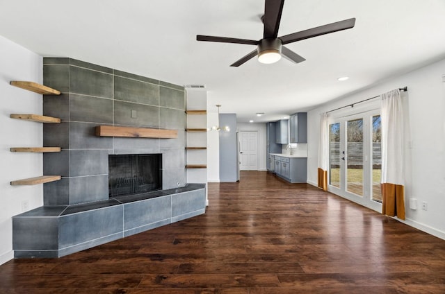 unfurnished living room with a sink, dark wood finished floors, baseboards, a ceiling fan, and a tile fireplace