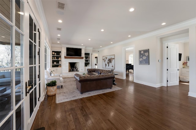 living area featuring crown molding, wood finished floors, visible vents, and a large fireplace