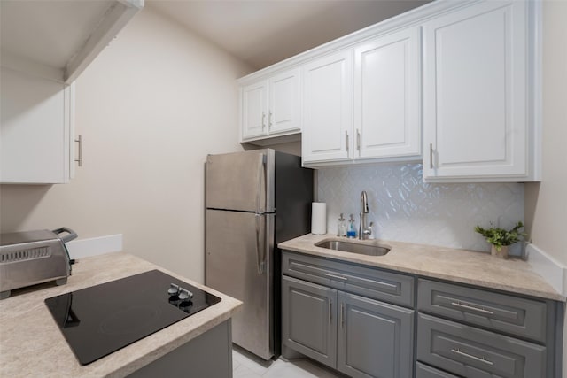 kitchen with gray cabinets, a sink, freestanding refrigerator, decorative backsplash, and black electric stovetop