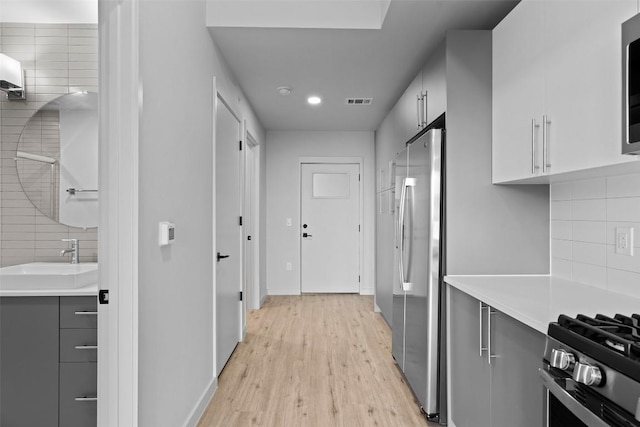 corridor featuring a sink, visible vents, baseboards, and light wood-style flooring