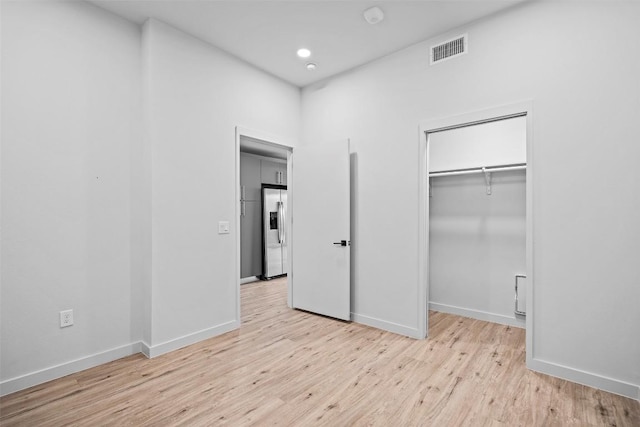 unfurnished bedroom with light wood-type flooring, visible vents, a closet, stainless steel fridge with ice dispenser, and baseboards