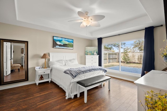 bedroom featuring baseboards, a raised ceiling, and dark wood-type flooring