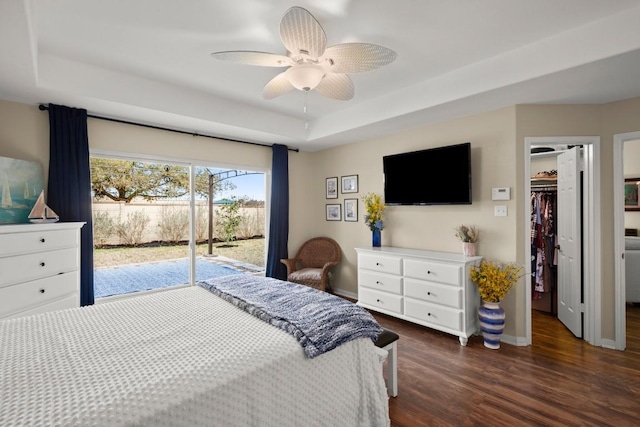 bedroom with baseboards, dark wood finished floors, a tray ceiling, access to exterior, and a walk in closet