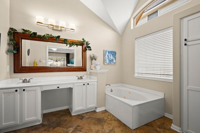 bathroom featuring lofted ceiling, a jetted tub, double vanity, and a sink