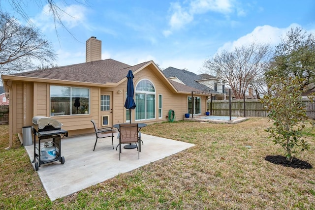 rear view of house with a patio, fence, a yard, roof with shingles, and a chimney