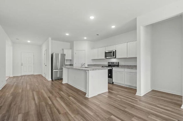 1424 Morris Loop, San Marcos, TX 78666 - kitchen with stainless steel appliances, a sink, wood finished floors, white cabinets, and a center island with sink