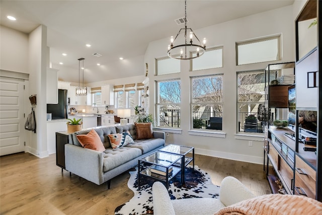 living area featuring visible vents, a notable chandelier, high vaulted ceiling, wood finished floors, and baseboards