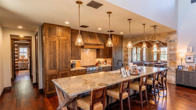 kitchen with high end stove, dark wood-type flooring, premium range hood, a breakfast bar, and a sink