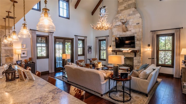 living room featuring beam ceiling, a stone fireplace, dark wood-type flooring, and an inviting chandelier