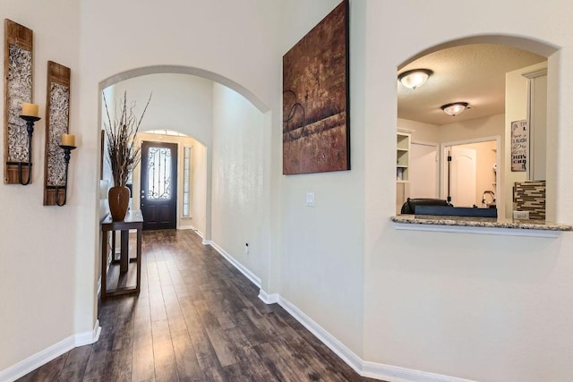 hallway featuring dark wood-style floors, arched walkways, a textured ceiling, and baseboards