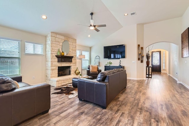 living room with wood finished floors, visible vents, arched walkways, a stone fireplace, and vaulted ceiling