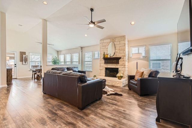 living area with a ceiling fan, lofted ceiling, a stone fireplace, and wood finished floors