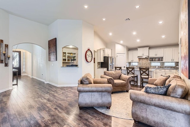 living room with visible vents, dark wood-style floors, arched walkways, and baseboards