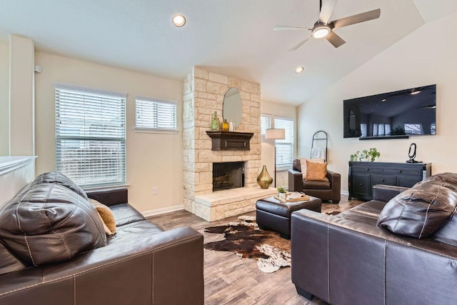 living room featuring lofted ceiling, wood finished floors, a stone fireplace, baseboards, and ceiling fan