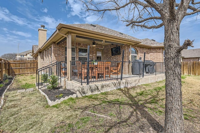 rear view of house featuring brick siding, a chimney, a fenced backyard, a patio area, and a ceiling fan