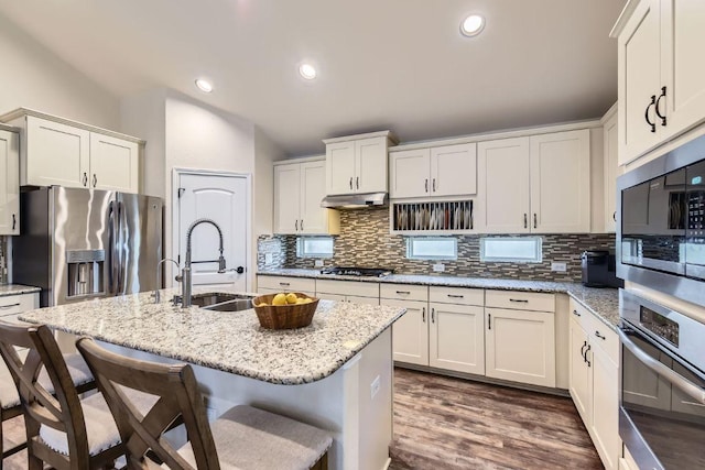 kitchen featuring under cabinet range hood, a kitchen bar, decorative backsplash, stainless steel appliances, and a sink