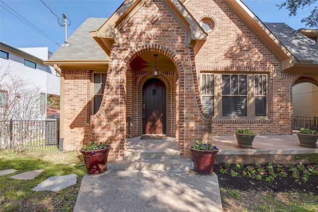 doorway to property with fence, brick siding, and a shingled roof