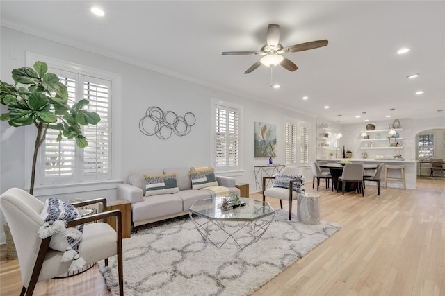 living room featuring arched walkways, recessed lighting, light wood-style floors, and ornamental molding