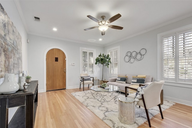 living room with arched walkways, visible vents, light wood finished floors, and ornamental molding