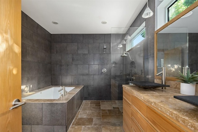 bathroom featuring vanity, a garden tub, stone tile flooring, a walk in shower, and tile walls