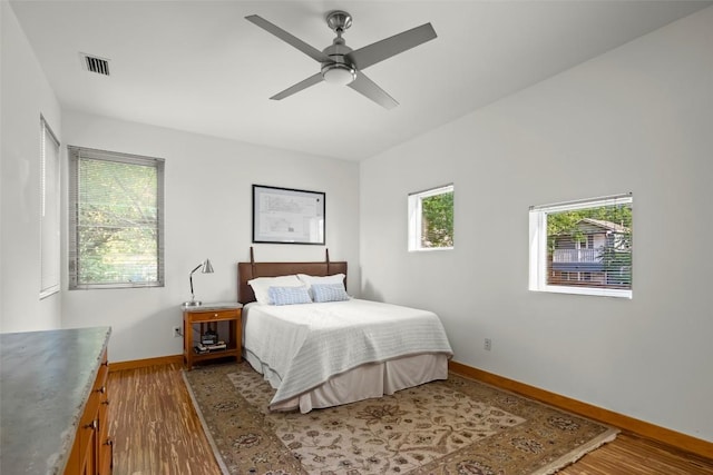 bedroom featuring a ceiling fan, wood finished floors, visible vents, and baseboards