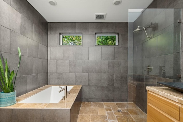 full bathroom with visible vents, walk in shower, a garden tub, stone tile floors, and tile walls