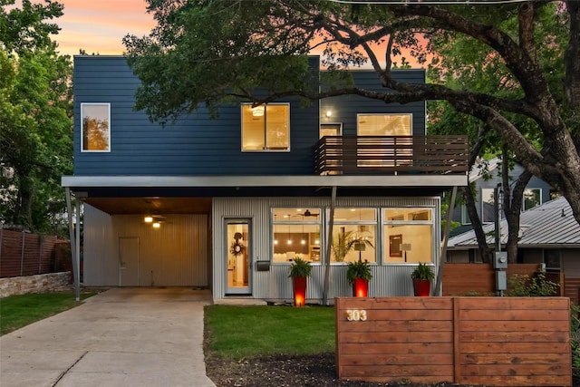 view of front of home with a carport, a balcony, fence, and driveway