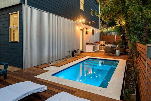 view of pool featuring a deck, a sink, fence, grilling area, and an outdoor kitchen