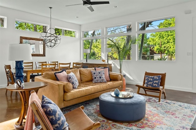 living room featuring ceiling fan with notable chandelier, baseboards, and concrete flooring