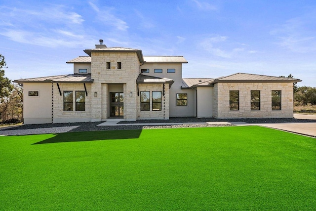 back of property featuring a lawn, a chimney, metal roof, stone siding, and a standing seam roof