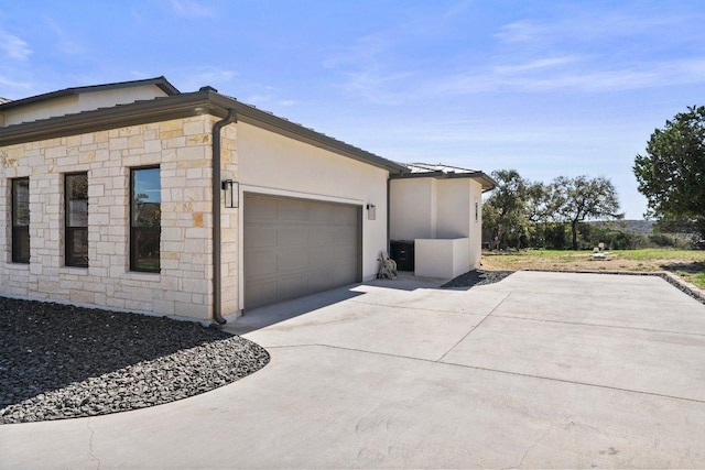 view of side of home featuring stone siding, stucco siding, concrete driveway, and a garage