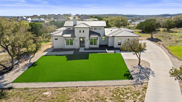 view of front facade featuring a front lawn, a chimney, metal roof, driveway, and a standing seam roof